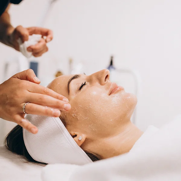 Une femme recevant un soin du visage dans un salon de beauté, détendue sur une table de traitement.