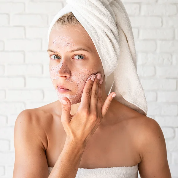 Une femme en serviette applique un masque facial sur son visage.
